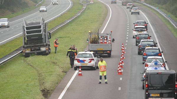 Lange file op A28 door vrachtwagen met containers in middenberm